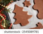 Tree and other shapes cut out from raw pastry dough on a sheet of baking paper - making homemade gingerbread Christmas cookies