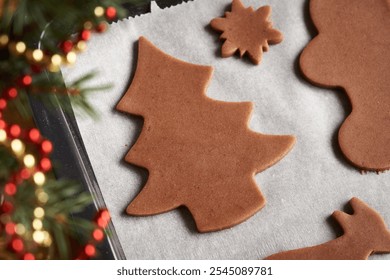 Tree and other shapes cut out from raw pastry dough on a sheet of baking paper - making homemade gingerbread Christmas cookies - Powered by Shutterstock