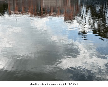 ​Sky and tree reflections on the rippling surface of a calm body of water.