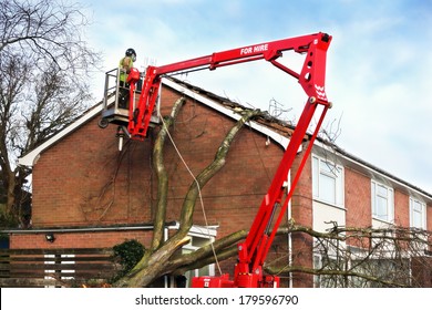 Tree Surgeon Working Up Cherry Picker Repairing Storm Damaged Roof After An Uprooted Tree Fell On Top Of A Residential House