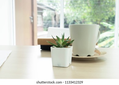 The tree is in a white vase and a white coffee cup is placed on the desk. - Shutterstock ID 1133412329