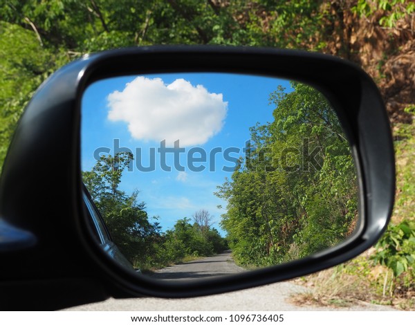 The trees\
and clouds reflected in the car\
mirror