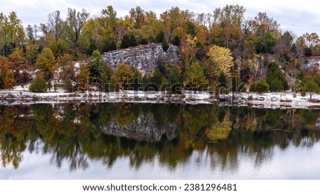 Trees and fall foliage on rocky bluffs reflected in the water of a lake at Klondike County Park in St. Charles County Missouri, USA