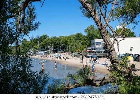 Trees framing view of sandy beach. Summer sunny day. Port Dover, Ontario, Canada. Great Lakes, Lake Erie freshwater water. People swimming playing relaxing. Recreation leisure fun. Destination.