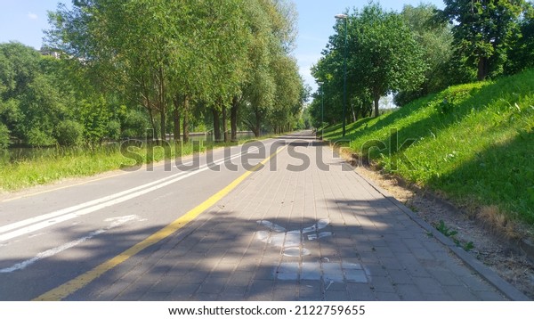 Trees grow\
along the riverbed that flows through the city, and paved bicycle\
and tiled pedestrian paths are laid, on which markings are applied.\
There are lighting poles along\
them.