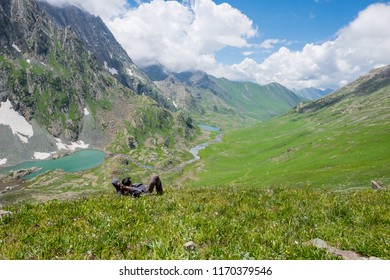 A trekker lie about on Gadsar lake and a meadow at kashmir great lakes trek in kashmir. Solo person in the mountains and lake of Kashmir, India. The breathtaking view of Krishansar lake on blue sky.