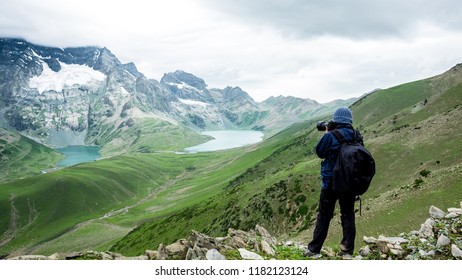 A trekker take photo at past Gadsar lake and a meadow at kashmir great lakes trek in kashmir. Solo person in the mountains and lake of Kashmir, India. The breathtaking view of lakes on blue sky.