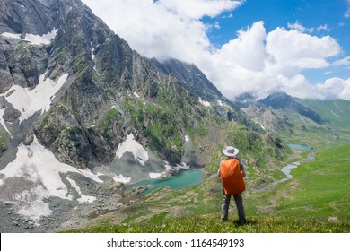 A trekker walks past Gadsar lake and a meadow at kashmir great lakes trek in kashmir. Solo person in the mountains and lake of Kashmir, India. The breathtaking view of Krishansar lake on blue sky.