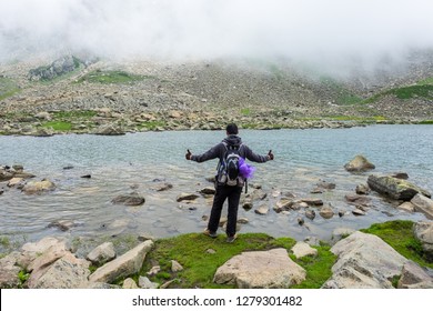 A trekker walks past Gadsar lake and a meadow at kashmir great lakes trek in kashmir. Solo person in the mountains and lake of Kashmir, India. The breathtaking view of Krishansar lake on blue sky.