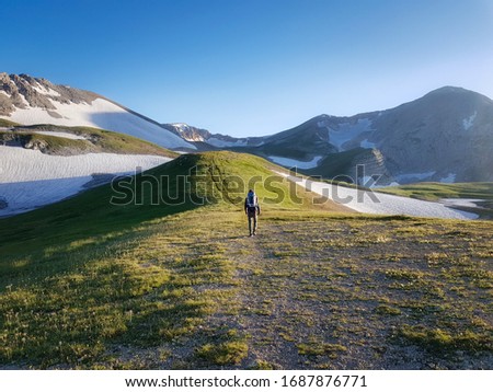 Trekking in mountains. Tourist with backpack goes up mountain road. Tourist goes up to Caucasus Mountains. Lagonaki, Fisht Oshten