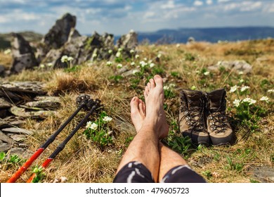 Trekking Shoes, Hiking Sticks And Bare Feet Of Resting Camper On Romantic Mountain Background