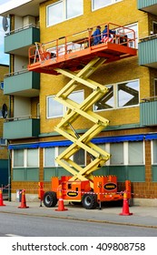 Trelleborg, Sweden - April 12, 2016: Workers On Top Of A Riwal Scissor Lift Platform Performing Some Window Repairs Outside An Apartment.