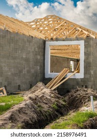 Trench for conduit in front of window opening of single-family house under construction, with wooden roof trusses on concrete shell, in a suburban development in southwest Florida