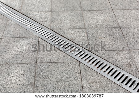 Trench drain gray with steel purification grate on granite stone tile road improvement of the city, close up details drainage system, nobody.