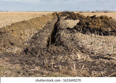 Trench Excavated In Farm Field With Piles Of Soil. Water Drainage Pipe, Field Tile Installation