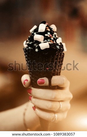 Trend cone of charcoal ice cream with Confetti and food powder, pink and blue fluffy sweet in women's arm. Blurred bokeh city background, Sunlight flare for text and design.
