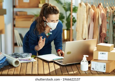 Trendy 40 Years Old Small Business Owner Woman With Ffp2 Mask, Parcel And Antiseptic Having Video Conference On Laptop In The Office.