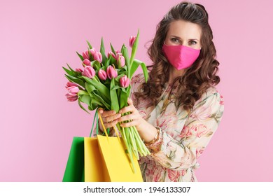 trendy 40 years old woman in floral dress with tulips bouquet, pink mask and shopping bags isolated on pink background. - Powered by Shutterstock