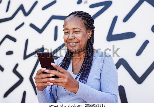 Trendy african american senior woman using\
mobile phone in the city with black and white background - Elderly\
black lady enjoy\
technology
