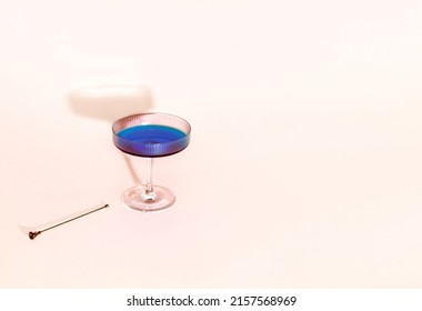 Trendy Art Deco glass, blue drink and cocktail skewer isolated against powdery pink background. Minimal creative summer holiday concept. Exotic refreshment. 
