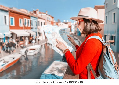 Trendy asian woman in hat looking for sights on a map near water channel in European town