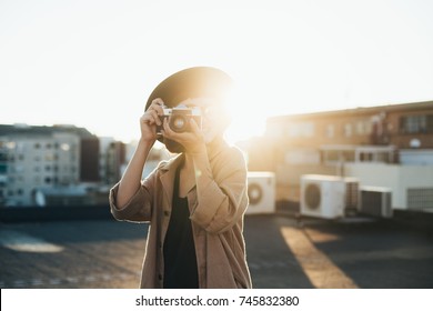 Trendy and attractive beautiful woman with analog vintage film camera makes photos on rooftop at sunset time, creates content for social media channels and applications, popular influencer - Powered by Shutterstock