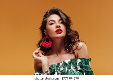 Trendy Attractive Woman With Wavy Hairstyle With Modern Cool Earrings And Big Red Lips In Green Sundress Looking Into Camera..