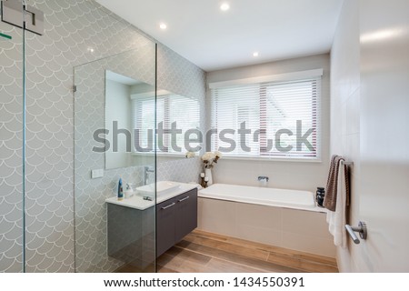 A trendy bathroom interior décor with a stylish all-white theme sink and bath tub, and a glass partition.