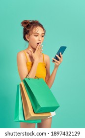 Trendy Beautiful Young Asian Woman Carrying Colorful Bags Shopping Online With Mobile Phone Isolated On Light Green Background