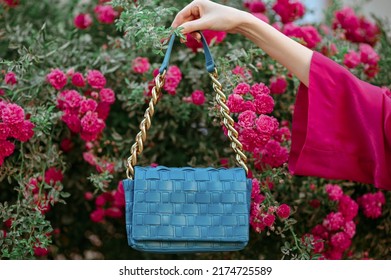 Trendy Blue Leather Wicker Bag, Purse. Summer Fashion Conception. Blooming Rose Garden As Background.  Copy, Empty Space For Text