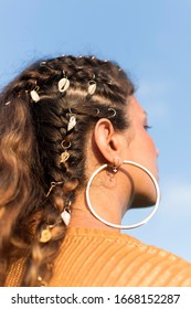 Trendy braided hairstyle with sea shells and gold hoops. Soft focus