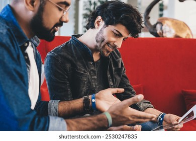 Trendy casual ethnic men having professional meeting in modern stylish cafe sitting at table with laptop and sharing printed pictures - Powered by Shutterstock