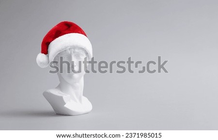Trendy christmas composition made of fake statue of David's head with red Santa Claus hat on light background. Minimal concept of new year. Creative art, minimal aesthetics. With copy space for text.