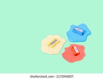 Trendy Composition With Colorful Pencil Sharpeners Dipped In Liquid On Olive Green Background. Surreal Office Or School Idea.