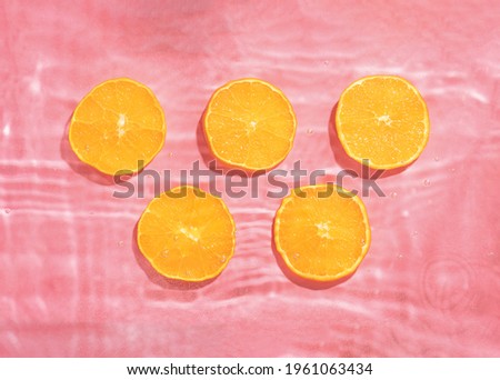 Trendy composition with five slices of orange fruit in pink splashy water. Sunny summer nature background.