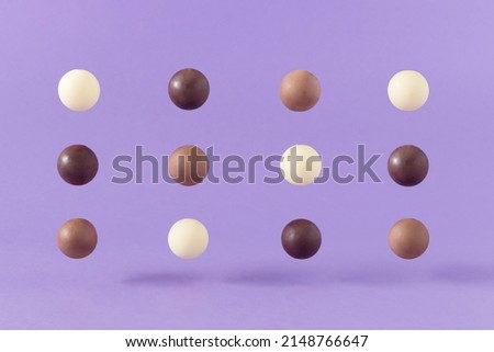 Trendy composition made of neatly arranged levitating brown, black and white chocolate balls against purple background. Minimal candy food concept. Creative dessert idea.