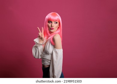 Trendy Cool Woman With Pink Hair Doing Peace Sign And Kissy Face In Front Of Camera. Carefree Attractive Girl Showing Victory Symbol And Peaceful Gesture With Two Fingers Up In Studio.