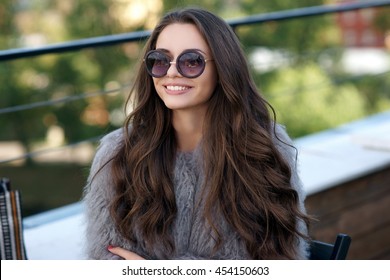 Trendy dressed fashionable girl wearing fur coat. Young pretty beautiful woman with long curly hair looking at you.