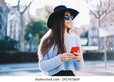 Trendy dressed female blogger with mobile technology smiling during leisure on vacations, happy Caucasian tourist enjoying getaway journey and time for media networking via smartphone gadget