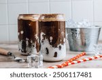 Trendy drink, Fluffy Coke, is a refreshing beverage made with cola, ice, and whipped marshmallows. A refreshing cola cocktail in two glass cups shaped like tin cans. Ice cubes and red paper straws.