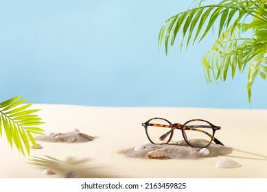 Trendy Eyeglass frame on beach with palm leaves, trendy Still Life Style. Tortoiseshell frame glasses on sand. Summer Optic store advertisement background. Copy space. Glasses sale concept. Eyeweare