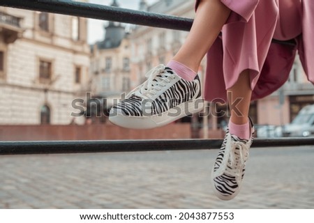 Trendy fashion details: woman wearing stylish sneakers with zebra print, posing in street of European city. Copy, empty space for text