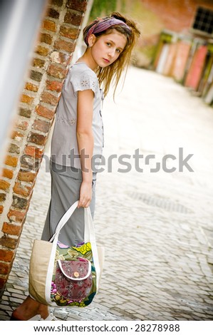 Trendy fashion teenager girl showing off new clothes and shopping bag against street background