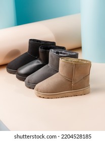 Trendy fashionable women's warm boots made of sheepskin of different colors on colored background. Side view of black, gray and beige warm uggs standing in row. Concept of winter women's shoes.
