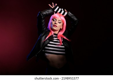 Trendy Female Rocker With Natural Leather Jacket And Pink Wig Psoing In Front Of Camera, Using Dark Lighting In Studio To Take Pictures. Feeling Attractive And Sensual, Carefree With Punk Fashion.