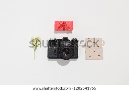 Trendy flat lay composition with retro camera, red gift box, gift canvas bag with red heart shapes and spring field flower on white background.