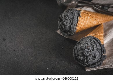 Trendy food. Black ice cream with black sesame, in traditional portioned ice cream cones. On a black stone table, in a wooden tray. Copy space