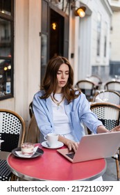 Trendy Freelancer Using Laptop Near Coffee And Dessert In Outdoor Cafe In Paris