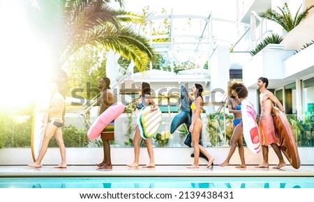 Trendy friends walking at swimming pool party with lilo airbed and swim wear - Vacation life style concept with happy guys and girls having fun on summer day at luxury resort - Bright vivid filter