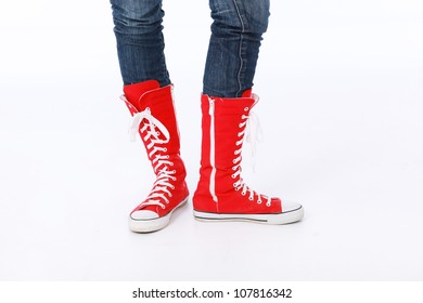 Trendy funky female or male hi top red canvas and white rubber boxing style trainer boots worn with blue jeans and facing forwards with one foot to side - Powered by Shutterstock